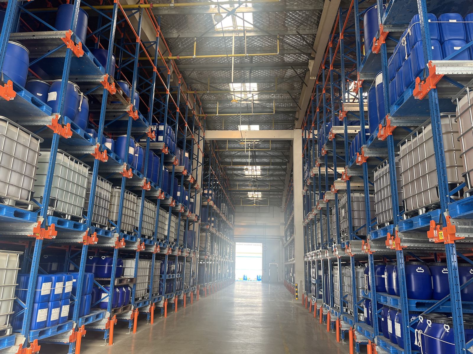 High racking holding IBC totes and blue plastic drums in a warehouse aisle