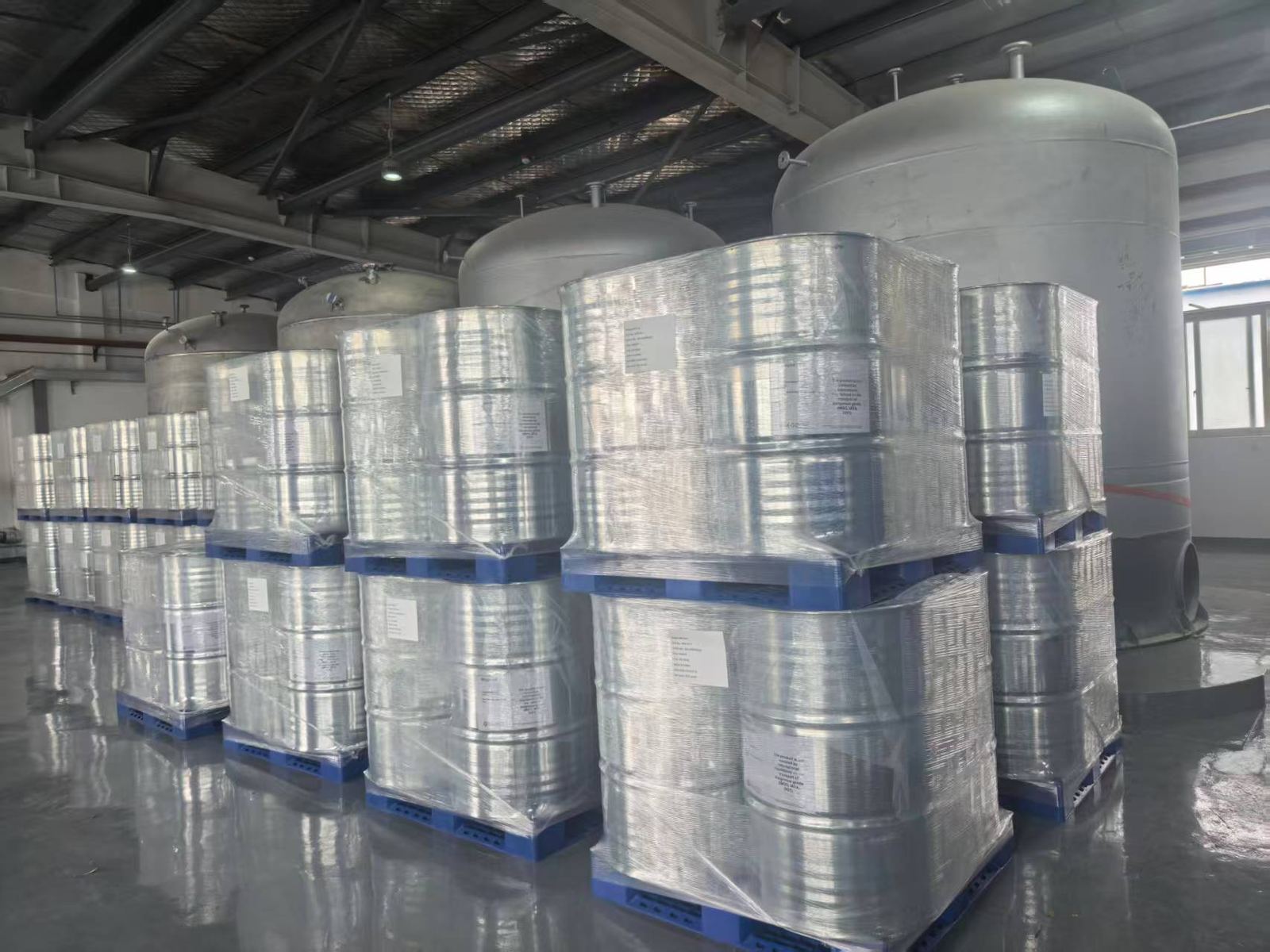 Steel drums on pallets, stretch-wrapped and labelled, in front of stainless steel storage tanks
